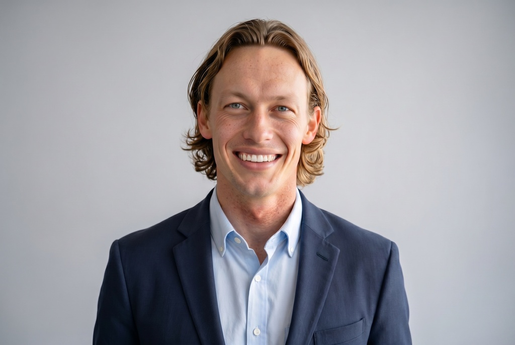 A professional ERAS headshot of a young medical applicant wearing a navy blazer over a light collared shirt, with a relaxed natural expression against a plain light gray studio background